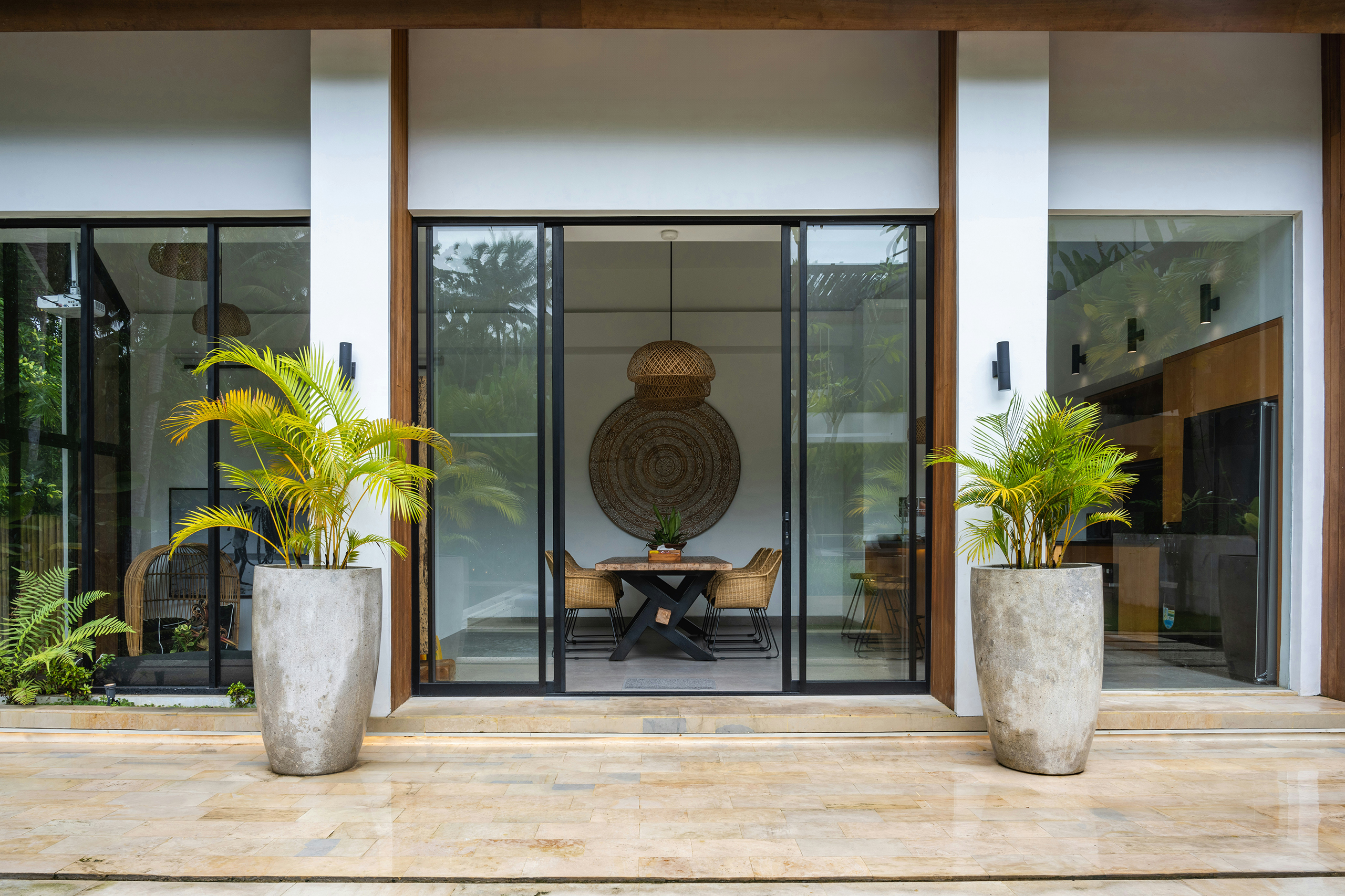 Entrada de casa moderna con ventanales de vidrio y decoración de interiores estilo feng shui, con plantas en macetas de cemento y mobiliario natural.