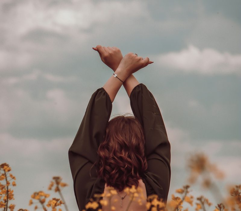 chica de espaldas con brazos cruzados levantados hacia el cielo nublado